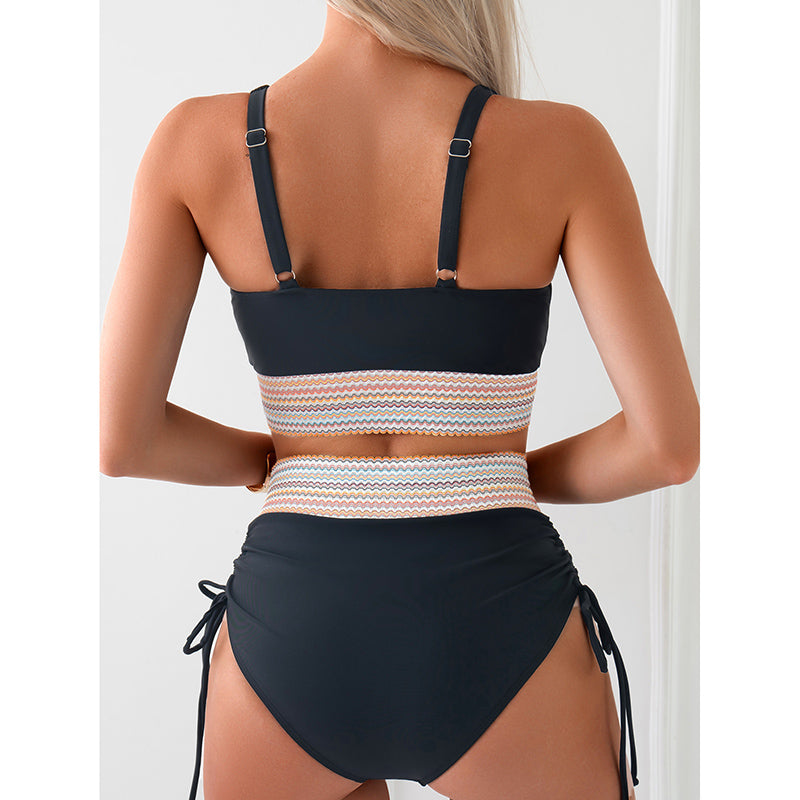 A woman is seen from the back wearing a high-waisted bikini with a color block design. The swimsuit features adjustable straps and a stylish zigzag pattern in the center, perfect for a confident beach or pool day.